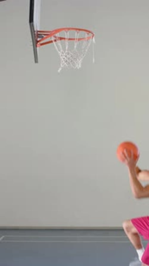 Vidéo verticale : en train de sauter au dunk basketball, un athlète masculin en tenue de sport atteignant un cerceau