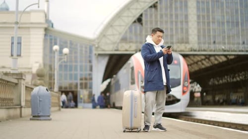 Man Standing at Train Station Using Smartphone