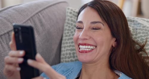 Woman Smiling Using Smartphone While Relaxing on Sofa