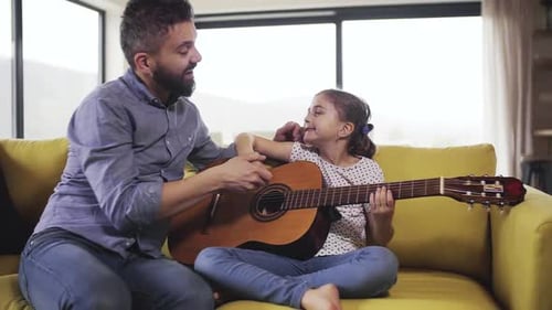 Father Helps Daughter Play Guitar on Couch