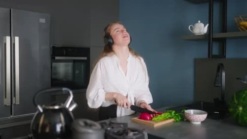 Woman in Headphones Making a Salad of Vegetables and Has Fun Dancing at Modern Kitchen Island Young