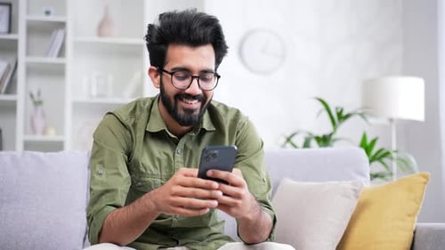 Young Adult Using Smartphone on Couch, Smiling