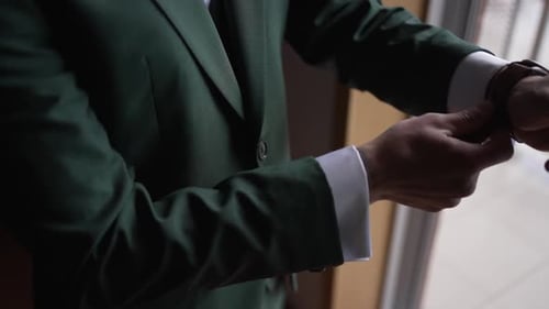 Man adjusting his wristwatch while wearing a green suit jacket and wedding ring