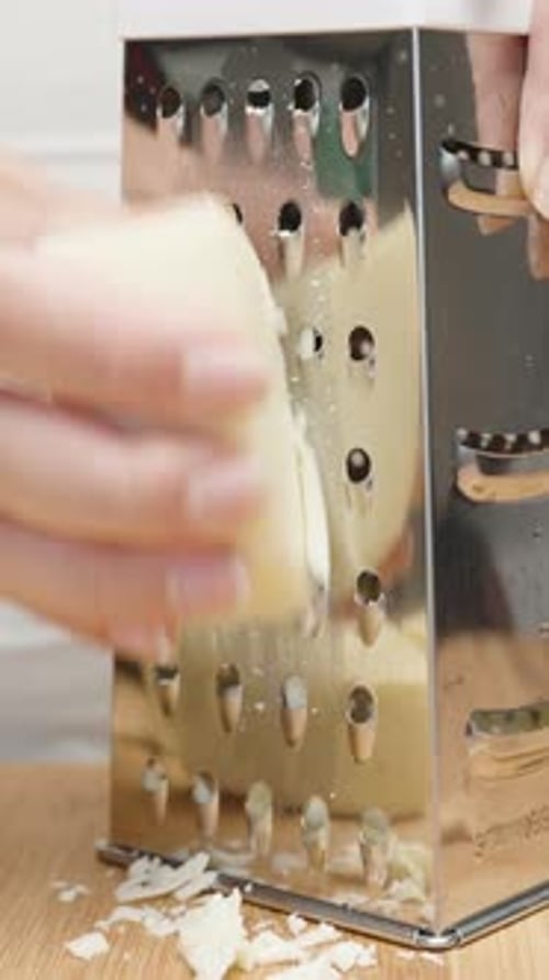The girl rubs cheese on a metal grater, close-up, the camera moves in a circle. slow motion Vertical