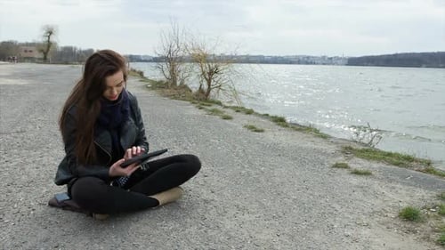 Woman Uses Tablet by Water on Overcast Day