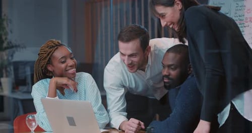 Four Young Multicultural People Sitting at Meeting Table and Looking at Laptop in Modern Office with