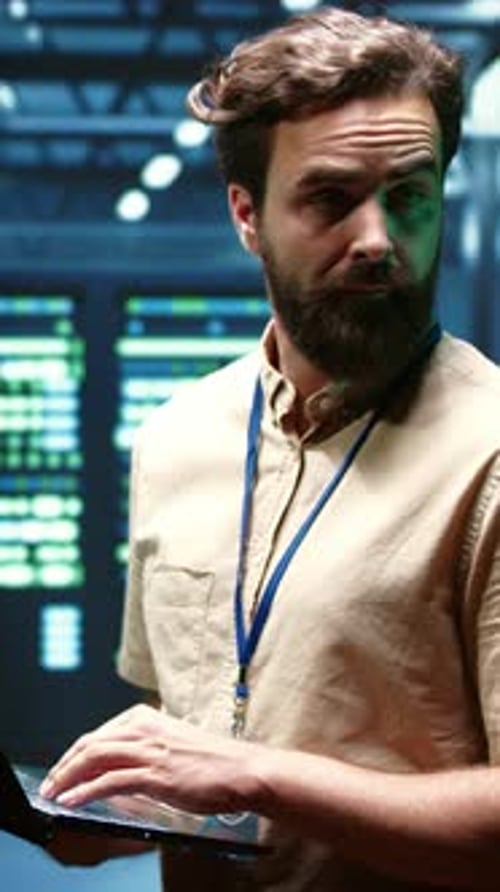 Bearded IT Technician Typing on Laptop in High-Tech Data Center