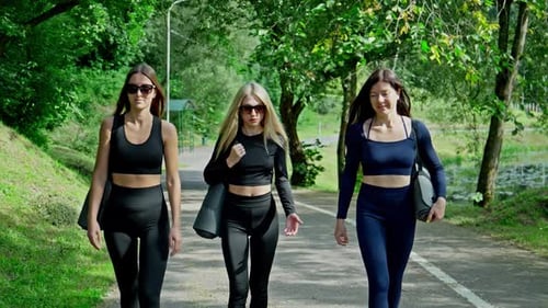 Three Friends Walk Together in Park Under Sun Dressed in Athletic Wear
