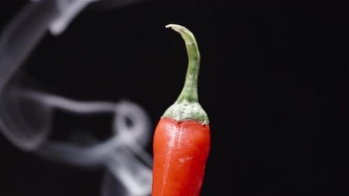 The tip of the red pepper rotates on a black background, it burns and there is Smoke, close-up