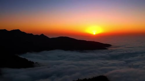 Dark mountain silhouettes in the thick white cloudscape. Beautiful setting sun in the orange sky