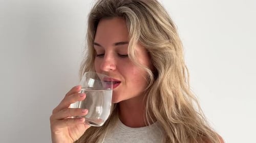 Woman Drinks Water in Front of White Wall