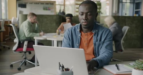 African American Businessman Typing with Laptop Working at Desk in Coworking Center