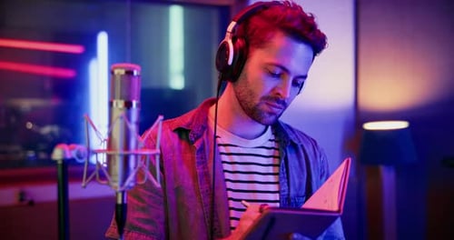 Young Male Musician Writing Song Lyrics in a Neon Lit Recording Studio