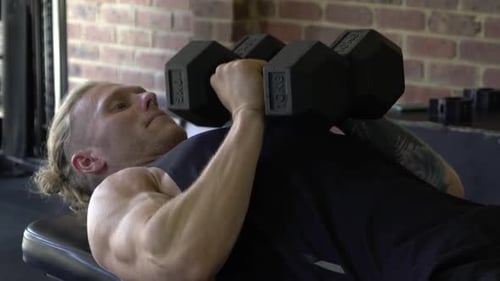 Muscly man in home gym exercising close grip dumbbell tricep bench press
