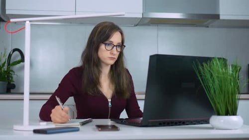 Confident Businesswoman Works From Home Office Typing on Laptop and Jotting Notes with Pen in