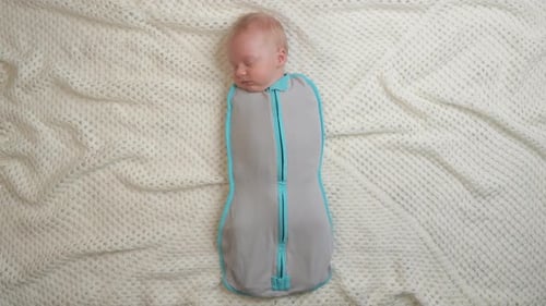 Infant Sleeping Peacefully in Swaddle Sack on Blanket
