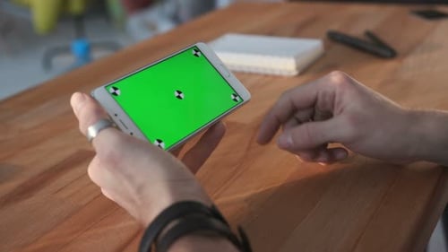 Hand scrolls on smartphone with green screen at desk