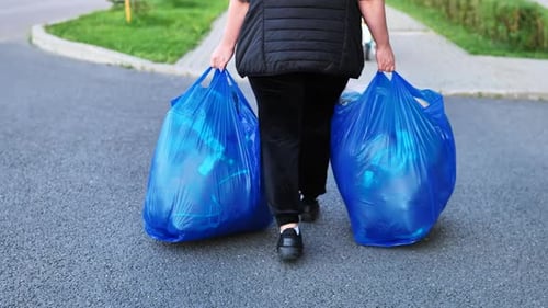 Persona que lleva dos bolsas azules grandes para tirar basura o reciclar al aire libre