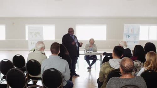 Man Talking To Audience At Community Town Hall Meeting