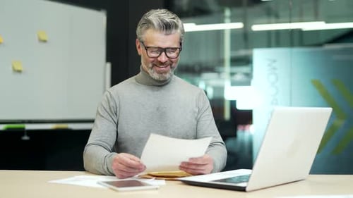 Mature Man Reviews Paperwork at his Desk