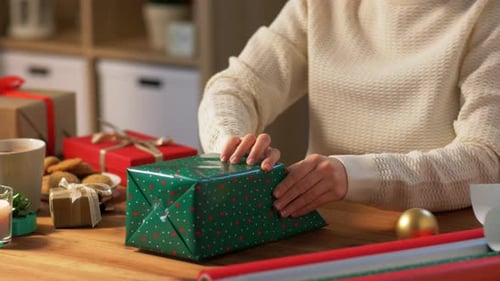 Holidays, New Year And Christmas Concept - Woman Wrapping Gift Box Into Green Paper At Home
