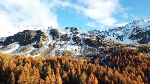 Aerial view of a mountainous landscape with snow-capped peaks and a forest of autumn-colored trees u