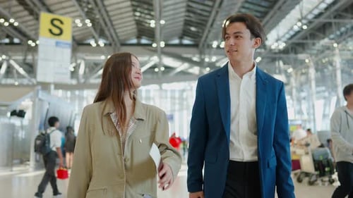 Asian businessman and woman walking in airport terminal to boarding gate.