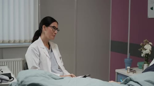 Caring Female Doctor Talking to Elderly Female Patient in Well-Equipped Ward