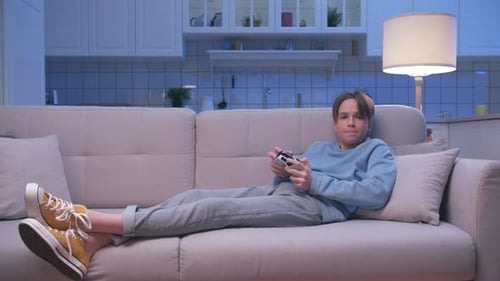 Teen Relaxing, Playing Video Game on Couch at Home