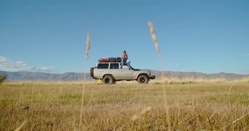 Adventurer Standing on Vehicle in Remote Field