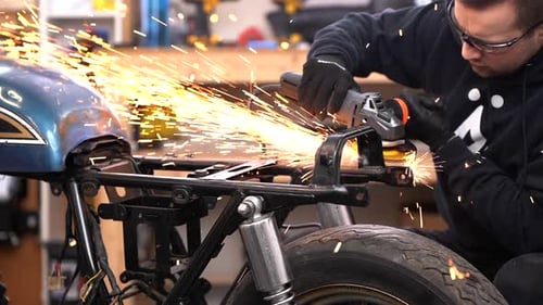 Young man cutting motorcycle metal frame with sparks flying