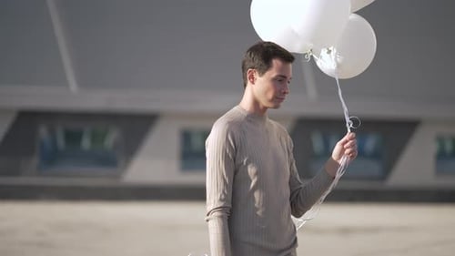 Young Man Holding White Balloons Outside