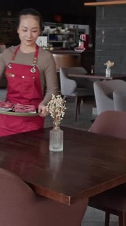 Female Cafe Employee Serving Tables with Plates and Napkins
