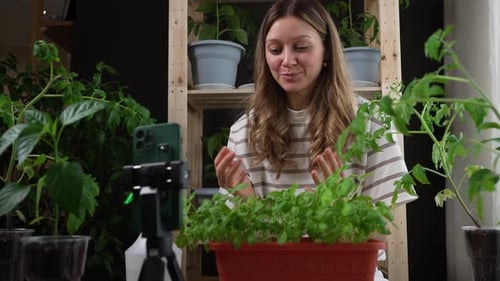 Young Woman Recording Gardening Tutorial with Smartphone Surrounded By Potted Plants in Home Studio