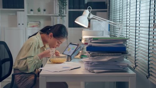 Asian young businesswoman eating noodles while work in office at night.