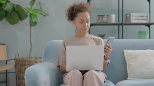 Woman on Couch Works with Laptop and Phone