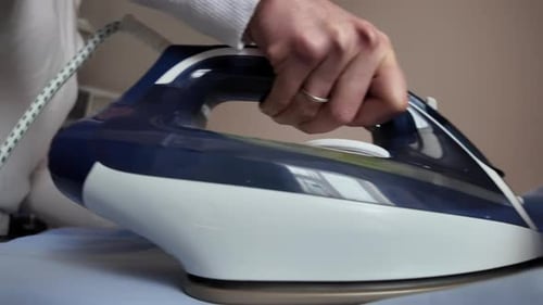 Close up woman ironing a blue shirt at home with white steam