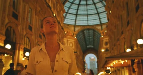 Mulher olhando para cima na Galleria Vittorio Emanuele II sob o teto de vidro à noite