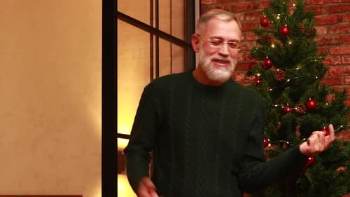 an Elderly Man in a Green Knitted Sweater Dancing Near the Christmas Tree