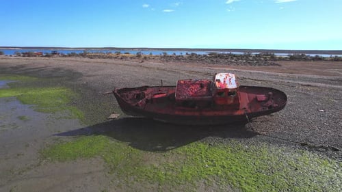 Kreisförmige Drohnenaufnahme eines zerstörten Fischerbootes, das verrostet ist und am Strand von Bahia Bustama liegt