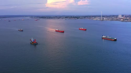 Panning Aerial view of Oil Tankers and Pertamina oil refinery in the background during sunset - Port