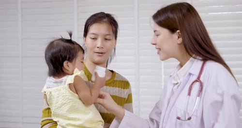 Asian mother with toddler interacting with smiling pediatrician during medical checkup in clinic,