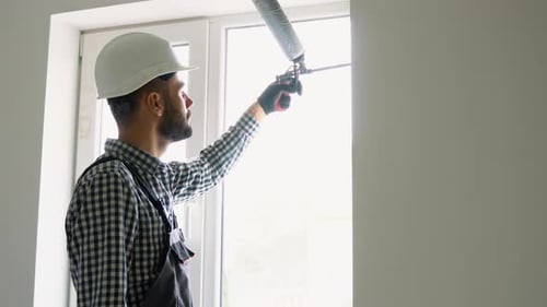 Latin Worker is Applying Polyurethane Foam to Fill Gap Between Sash and Window Frame