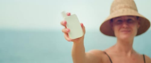 Woman holding sunscreen tube and shakes well before use. Girl on beach in sun hat, skin care SPF cre