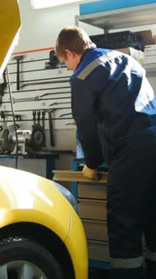 Automobile Service Mechanic Unscrews Detail of Car in Hood Slider