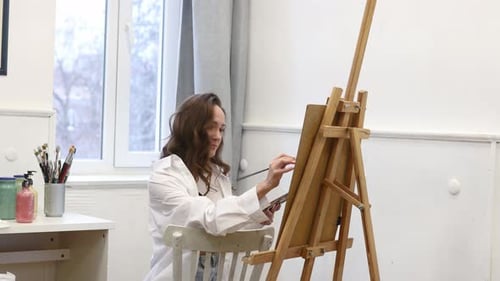 Young Female Artist Standing Near Easel and Holding Pencil While Working on Painting in Art Studio