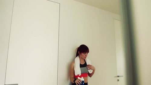 Young fitness woman drinking refreshing water after workout at home