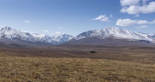 Timelapse of Sun Movement on Crystal Clear Sky with Clouds Over Snow Mountain Top Yellow Grass at