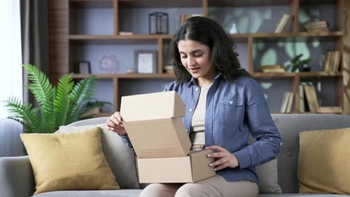 Joyful young female customer opens a package at home. Happy smiling woman buyer unpacking purchase