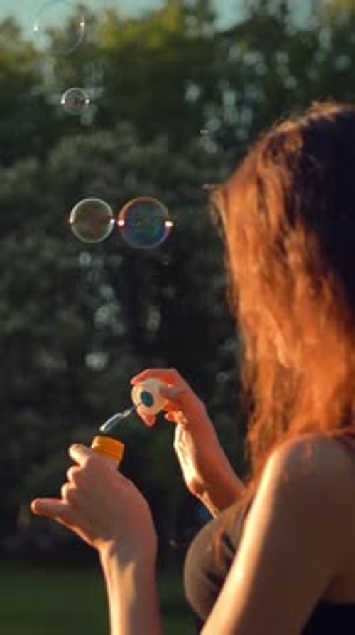 Vertical of Beautiful Young Redhair Lady Blow and Burst Soap Bubbles Outdoors